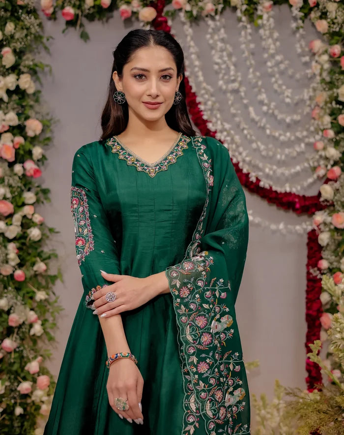 Woman in a green traditional outfit with floral patterns against a decorated background