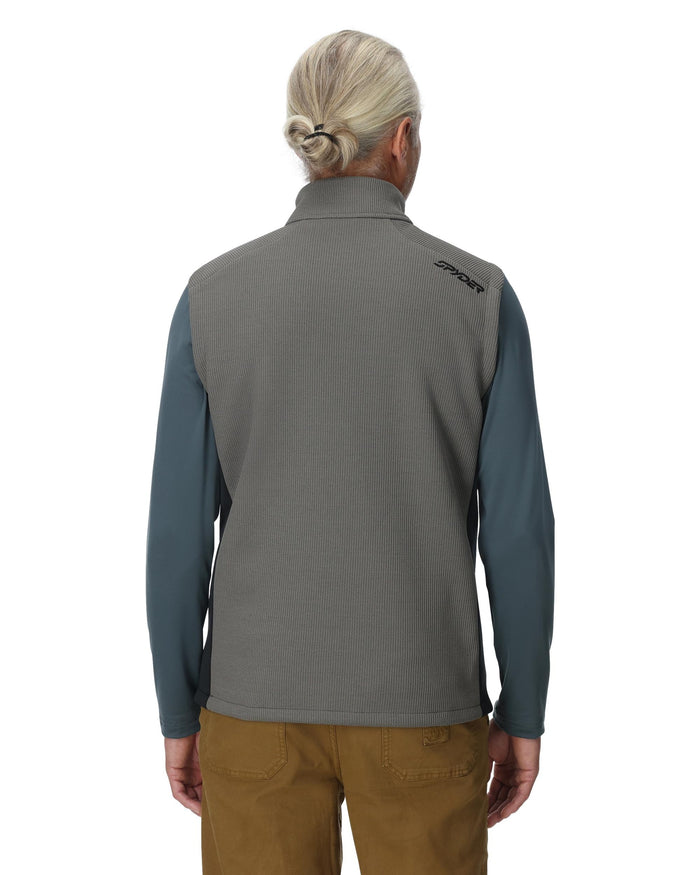 Person wearing a gray and blue pullover with a visible brand logo on the back, standing against a white background.
