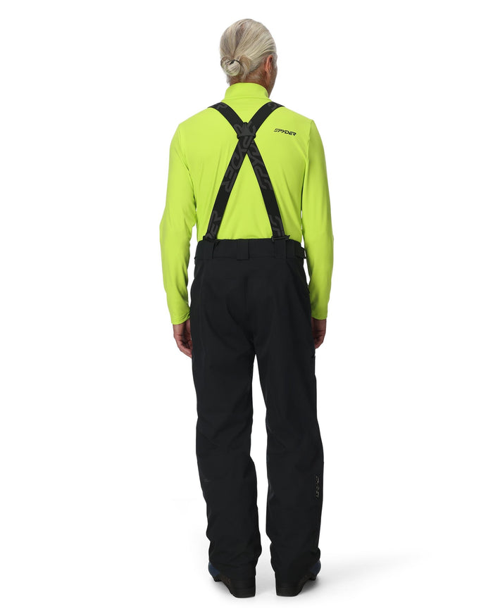 Person wearing a bright green jacket and black pants with suspenders on a white background