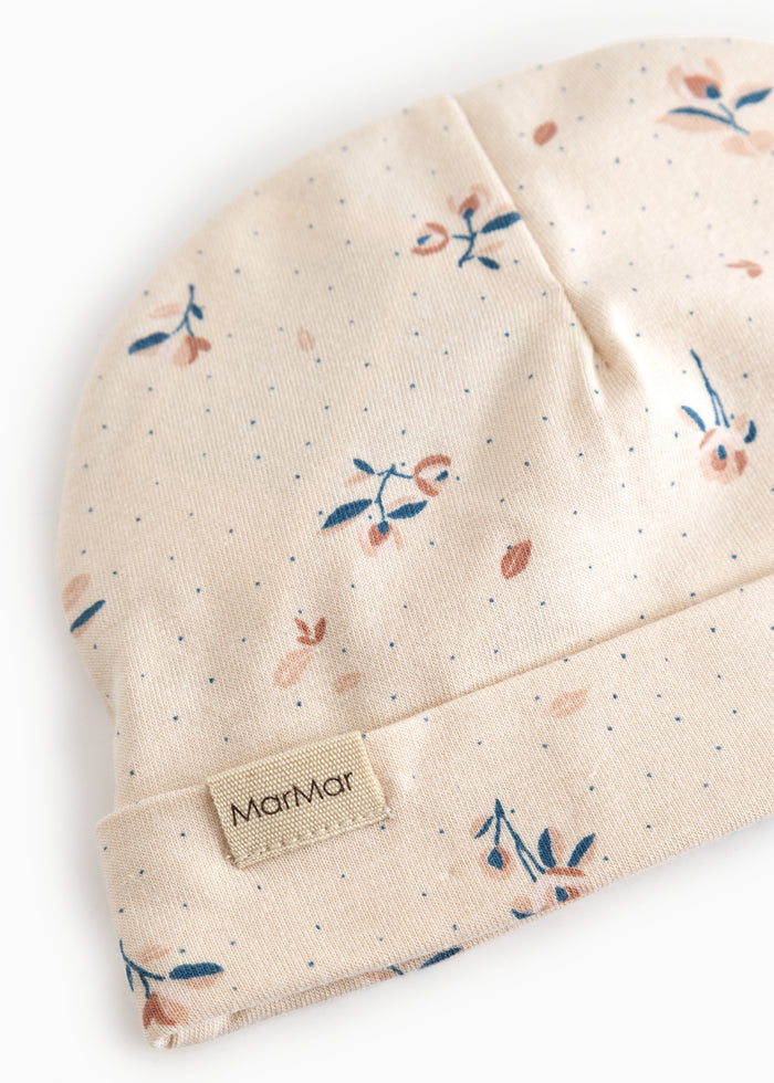 Beige babyhue med små blomsterprint og MARMAR-mærke ved foldet kant