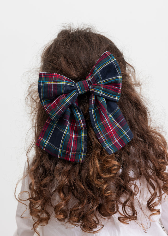 Girl with large checkered bow clip in her hair in Christmas-inspired dark blue, green and red shades