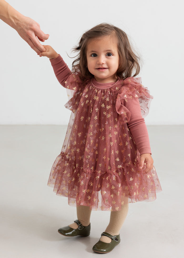 Baby wearing dusty pink bodysuit and festive pink patterned tulle dress