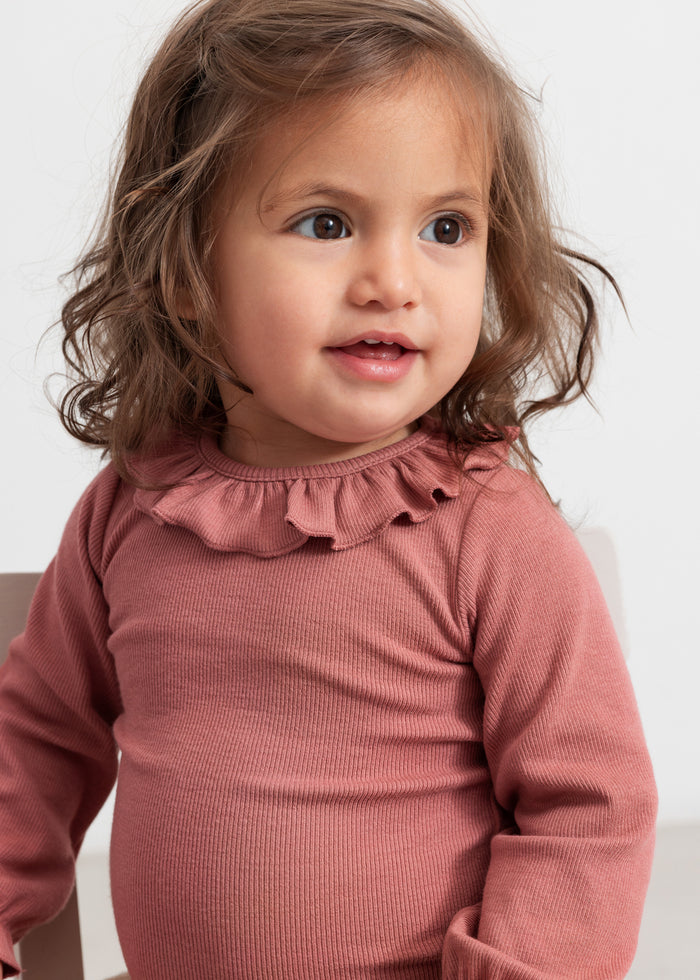 Baby wearing dusty pink bodysuit with ruffle collar