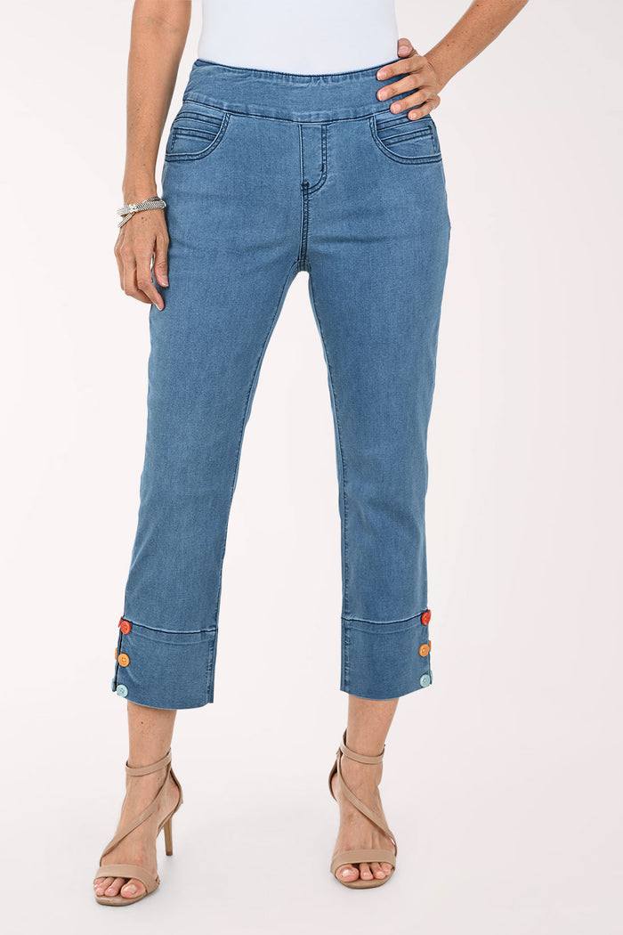 A model wearing blue cropped denim jeans with rolled cuffs featuring colorful button details, paired with beige high-heeled sandals against a plain white studio background.