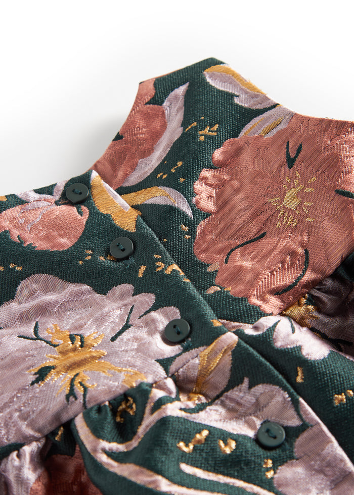 Close-up of dark green shiny fabric with floral print and golden details on baby's party dress