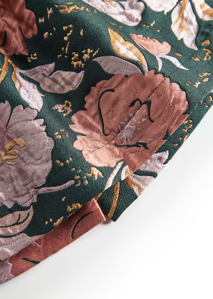 Close-up of dark green shiny fabric with floral print and golden details on baby's party dress