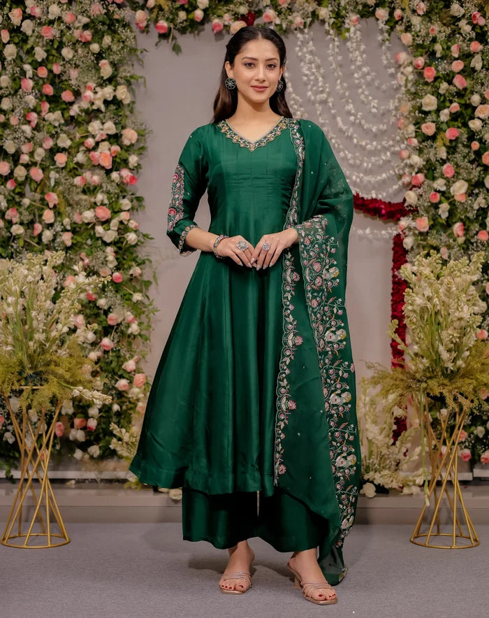 Woman in a green traditional outfit standing in front of floral decorations