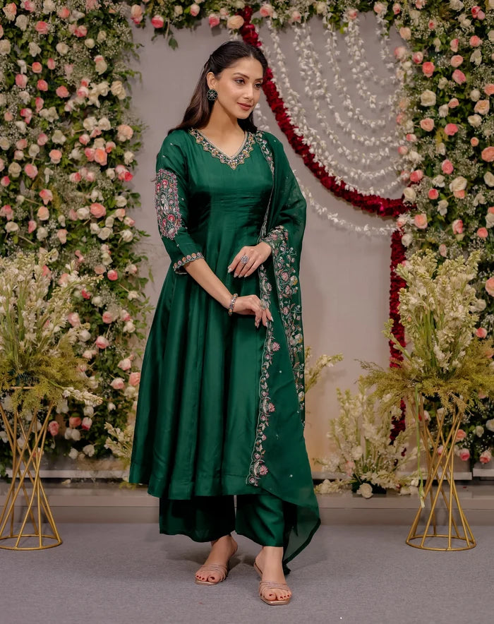 Woman in a green traditional outfit standing in front of floral decorations