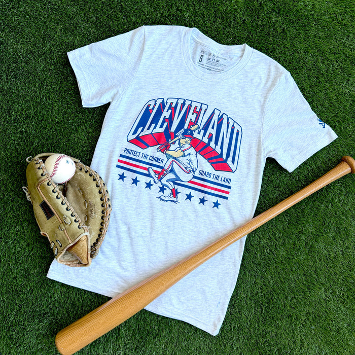 White t-shirt with Cleveland graphic design on grass, accompanied by a baseball, glove, and bat.