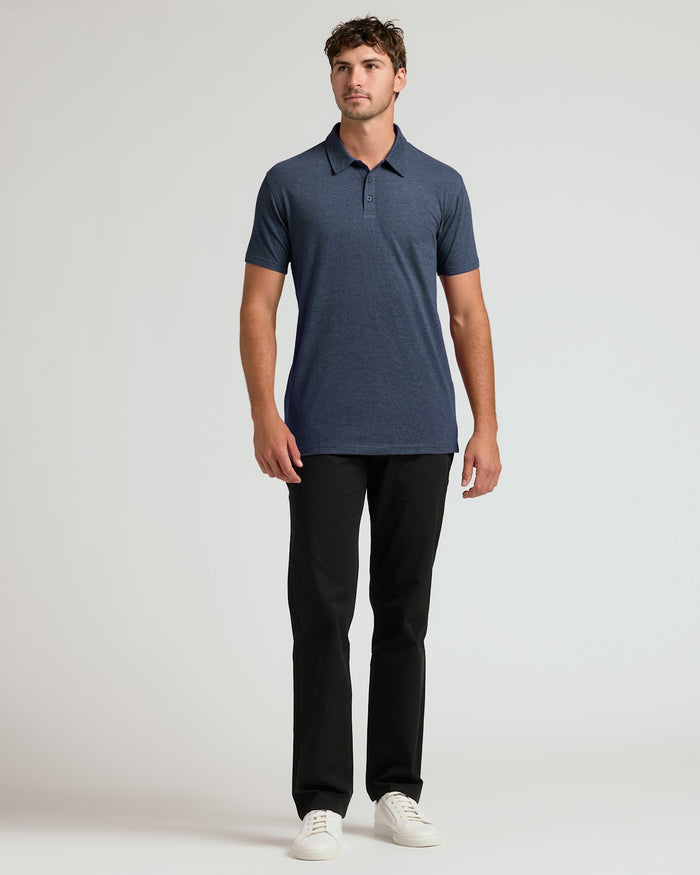 Man wearing a navy blue polo shirt and black pants on a light gray background