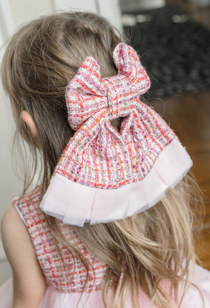 Kellie Pink Tweed Hair Bow styled in toddler’s hair, showcasing textured pink tweed fabric with subtle red threading and delicate layered tulle edge detail.