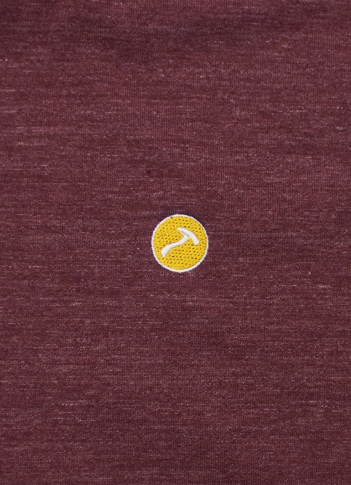 A small yellow circular patch with a white curved line is sewn onto the maroon LS Hooded Logo Tee.