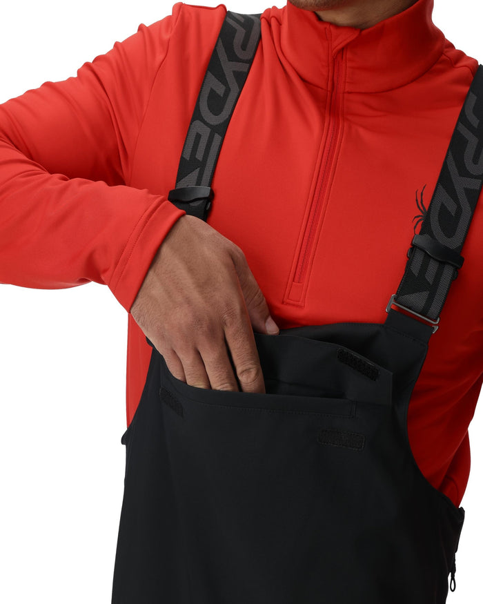 Person wearing a red jacket with a black backpack featuring a logo on a white background