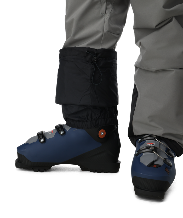 Blue ski boots with black gaiters worn by a person in gray pants on a white background