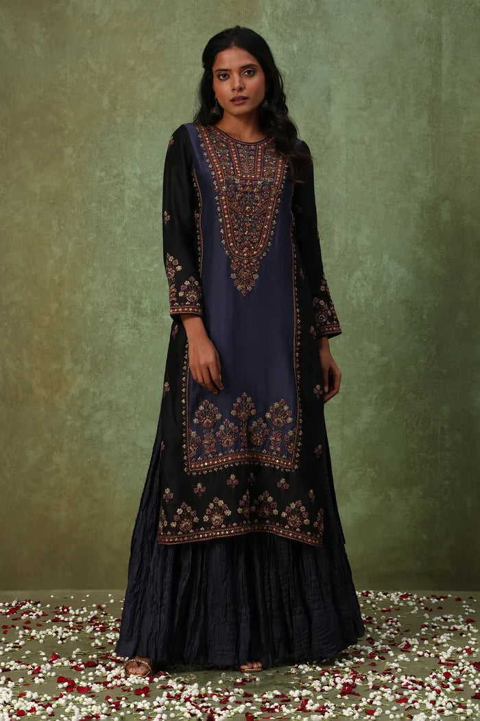 Woman wearing a black and blue embroidered traditional outfit on a textured green background.