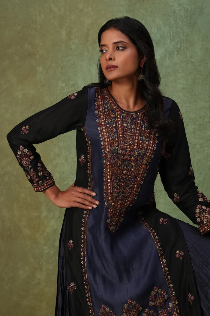Woman wearing a dark blue and black embroidered traditional outfit against a green background