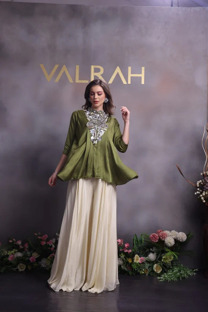 Woman in a green top and white skirt with 'VALRAH' branding in the background