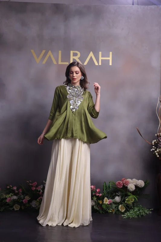 Woman in a green top and white skirt with 'VALRAH' branding in the background