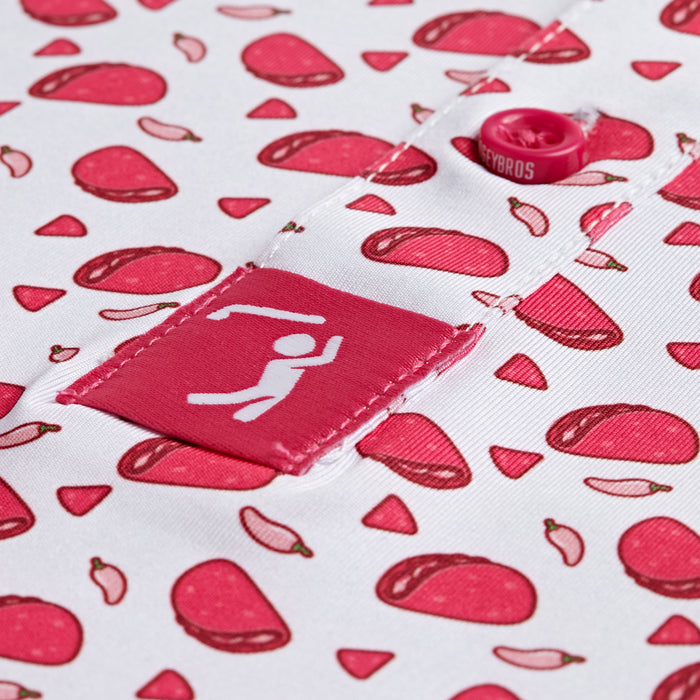 Close-up of the Pink Taco - Polo: a white shirt in an athletic fit with playful red meat and chili pepper prints. Features include a pink fabric tag with a swinging figure near the button placket, pink button, and partial text above the tag.