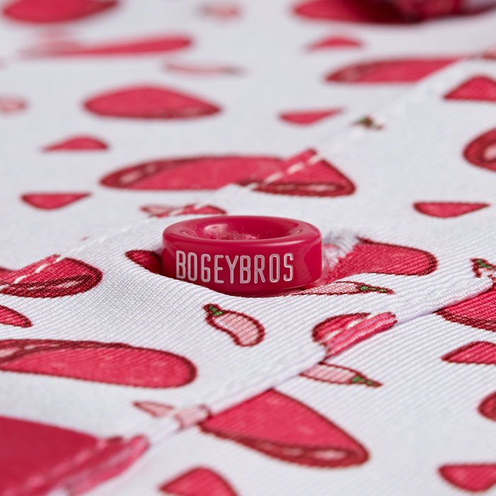 Close-up of Pink Taco - Polo, a white fabric with red chili peppers and meat slice pattern. Centered is a red button with BOGEYBROS in white. Features moisture wicking properties, visible stitching, and buttonhole detail.
