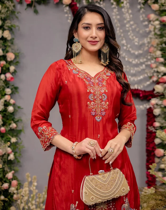 Woman in a red embroidered outfit holding a gold clutch against a floral decorated background