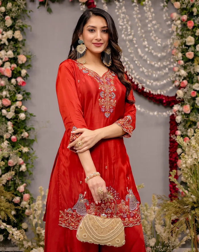 Woman in a red embroidered dress holding a gold purse against a decorated background