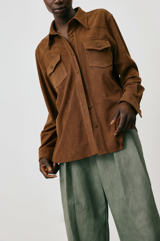 Person wearing a brown shirt and green pants on a white background