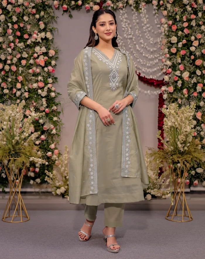 Woman in a light green traditional outfit standing in front of floral decorations