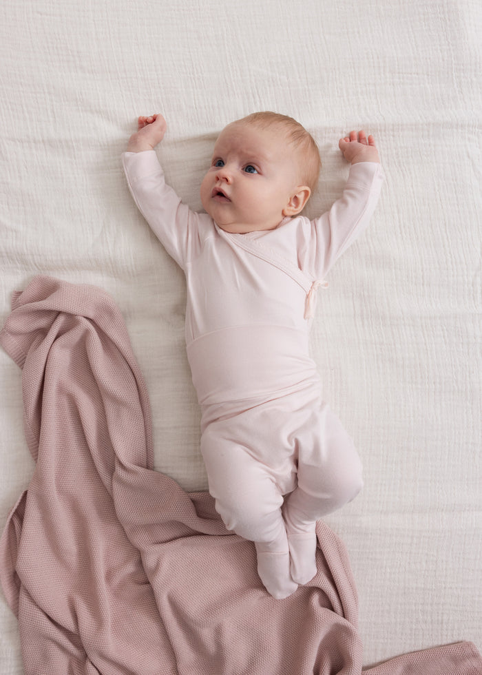 Lyserød tut-bluse med lange ærmer og slå-om forside med bånd, båret af baby