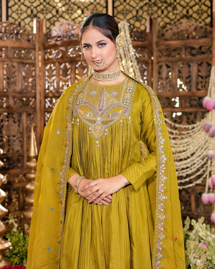 Woman in a yellow traditional outfit with intricate designs, standing against a decorative background.